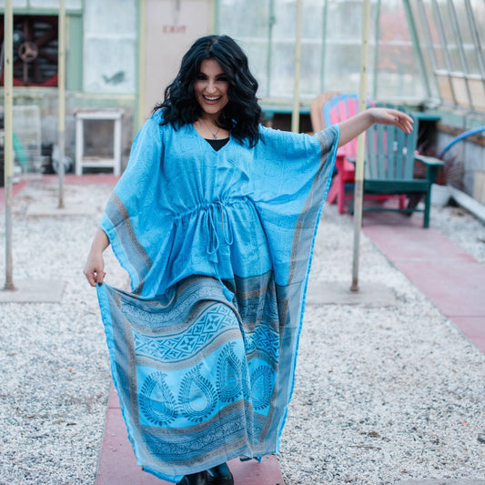 Model is dancing wearing a light blue aanya long kaftan while standing in a greenhouse.