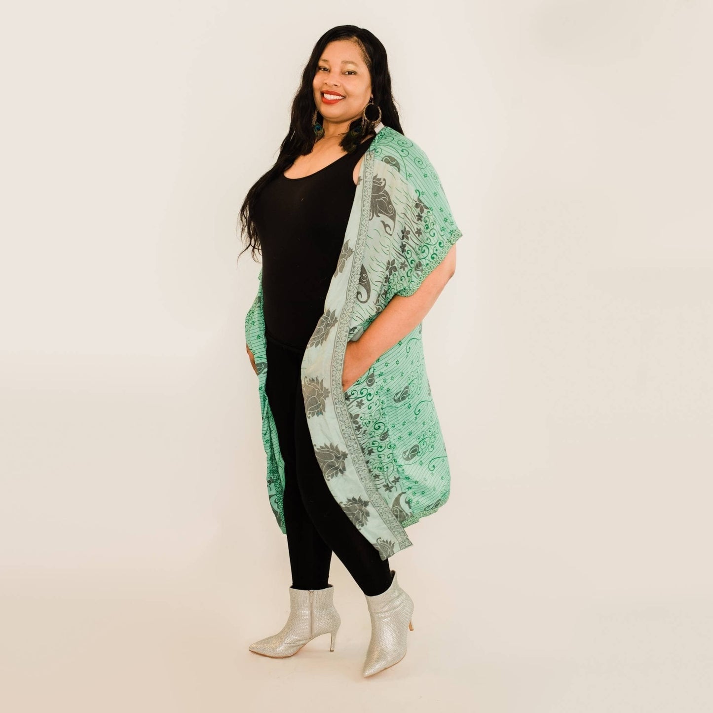 Plus size model has on a teal amara long duster while standing in front of a white backdrop.