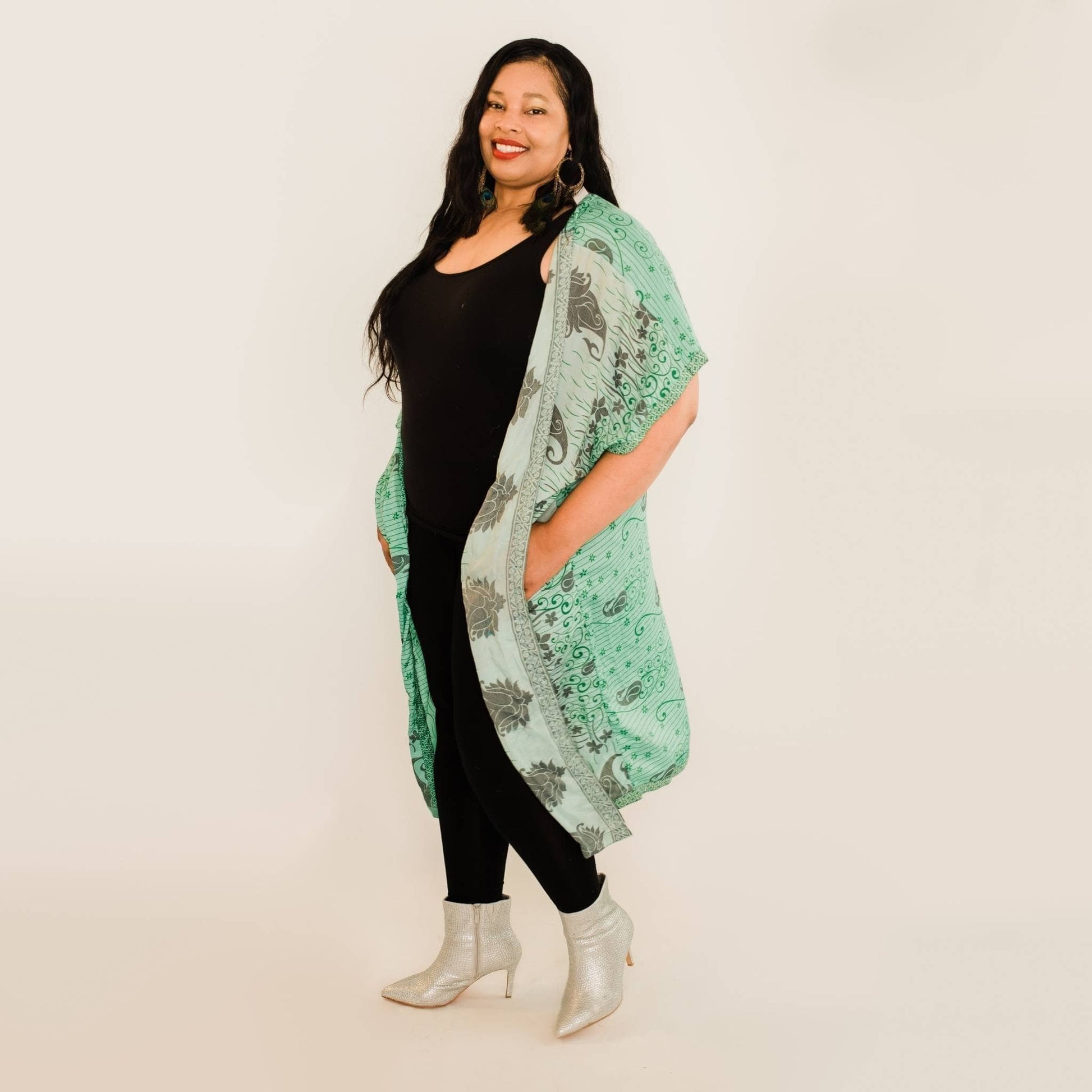Plus size model has on a teal amara long duster while standing in front of a white backdrop.