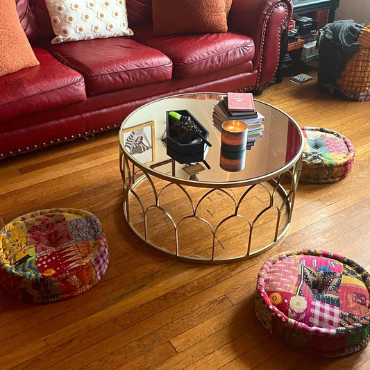 Three One of a Kind Hand Embroidered Pouf around a coffee table on a wooden floor.
