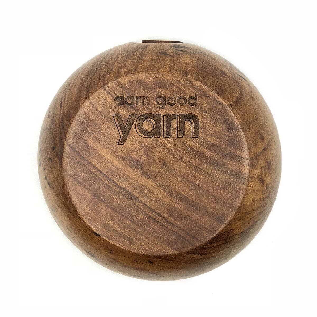 Bottom side of a wooden yarn bowl with etched Darn Good Yarn Logo sitting on a white surface
