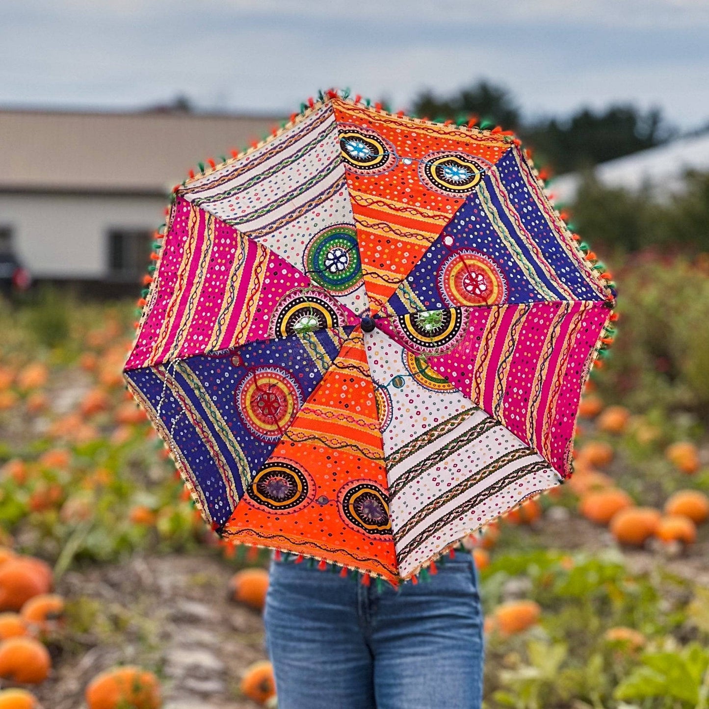 Model is holding a colorful Embellished Parasol Umbrella while standing in a pumpkin patch.