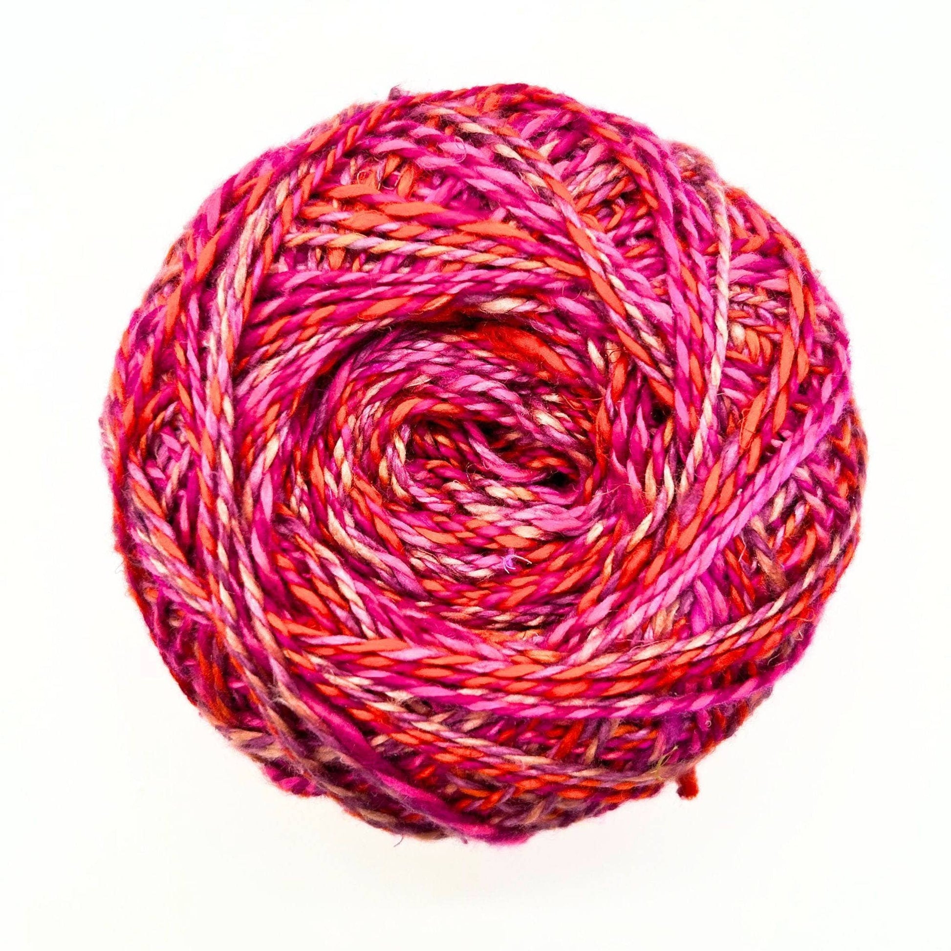 one skein of journey recycled silk yarn in the Field of Poppies colorway (variegated pink, orange, red) in front of a white background.