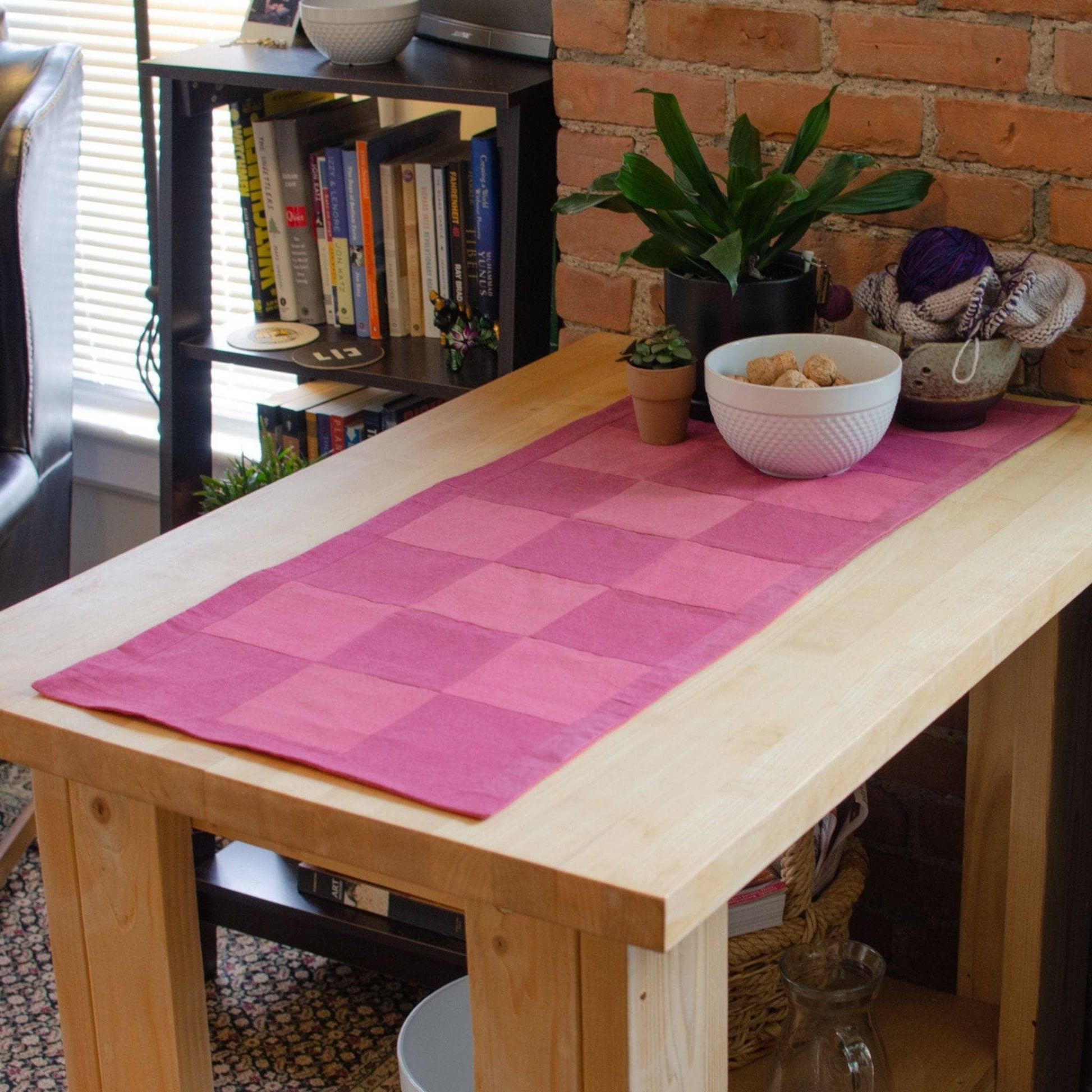Checkered pink table runner on wood table in front of an apartment background.