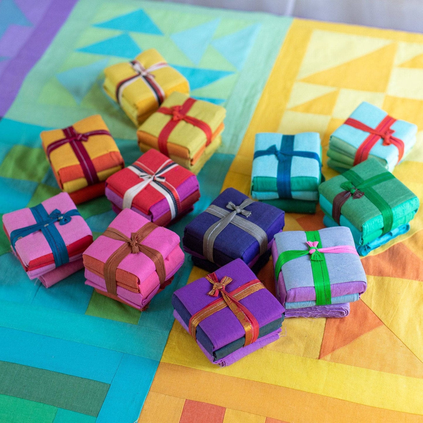12 cotton fat quarter packs stacked in two piles (left and right) sitting on blocks of a completed rainbow quilt kit.