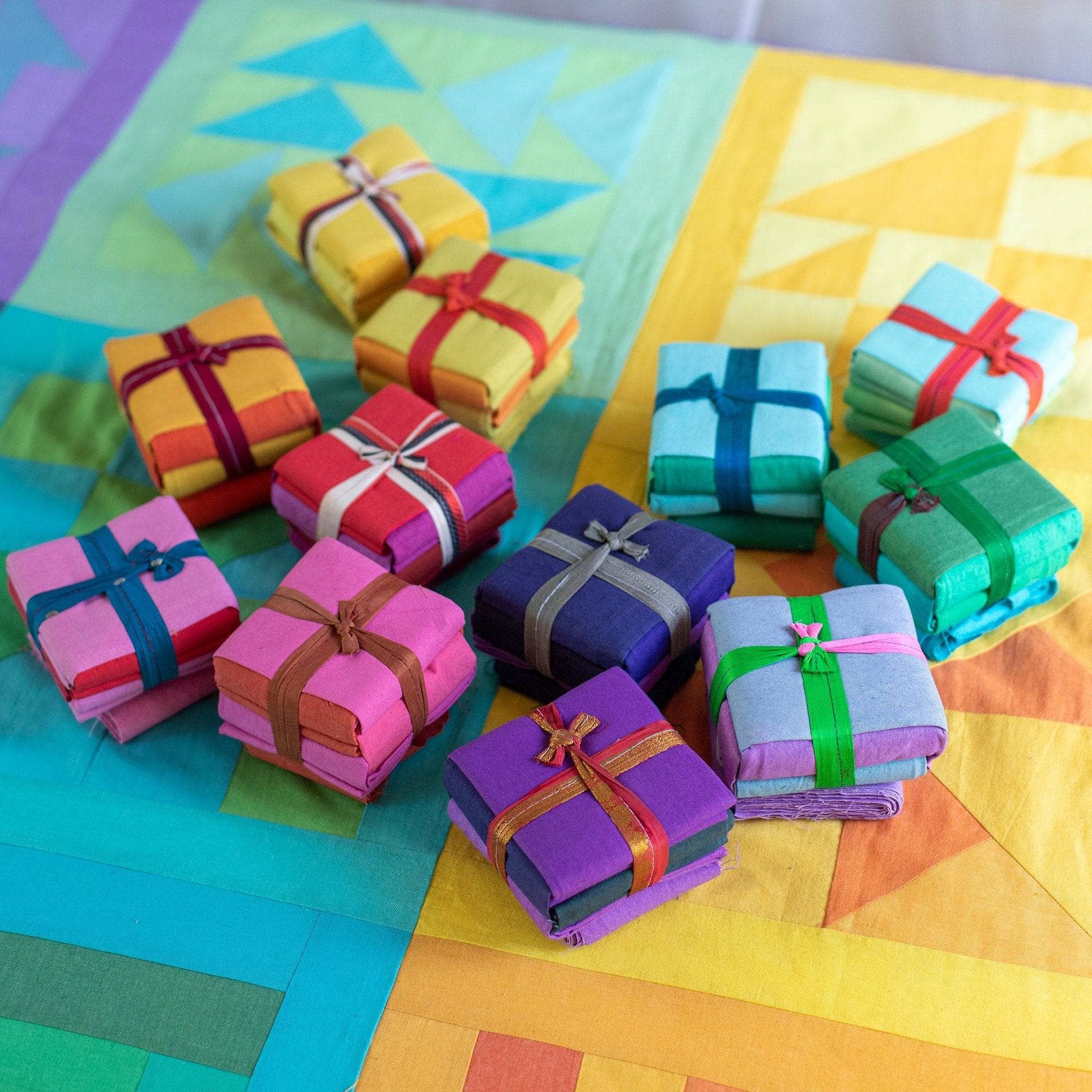 12 cotton fat quarter packs stacked in two piles (left and right) sitting on blocks of a completed rainbow quilt kit.