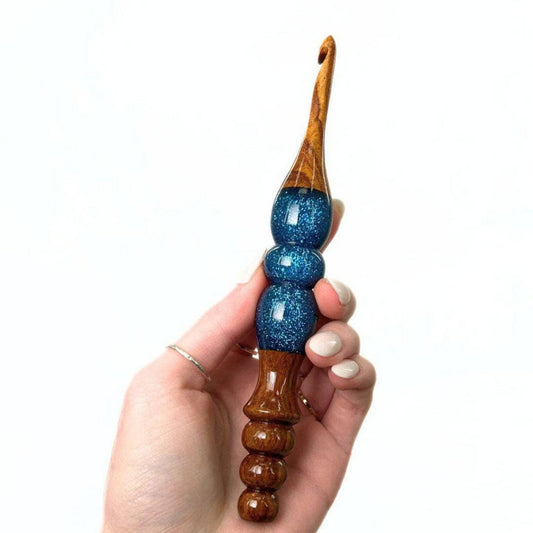 A woman's hand holing a wooden and resin crochet hooks.