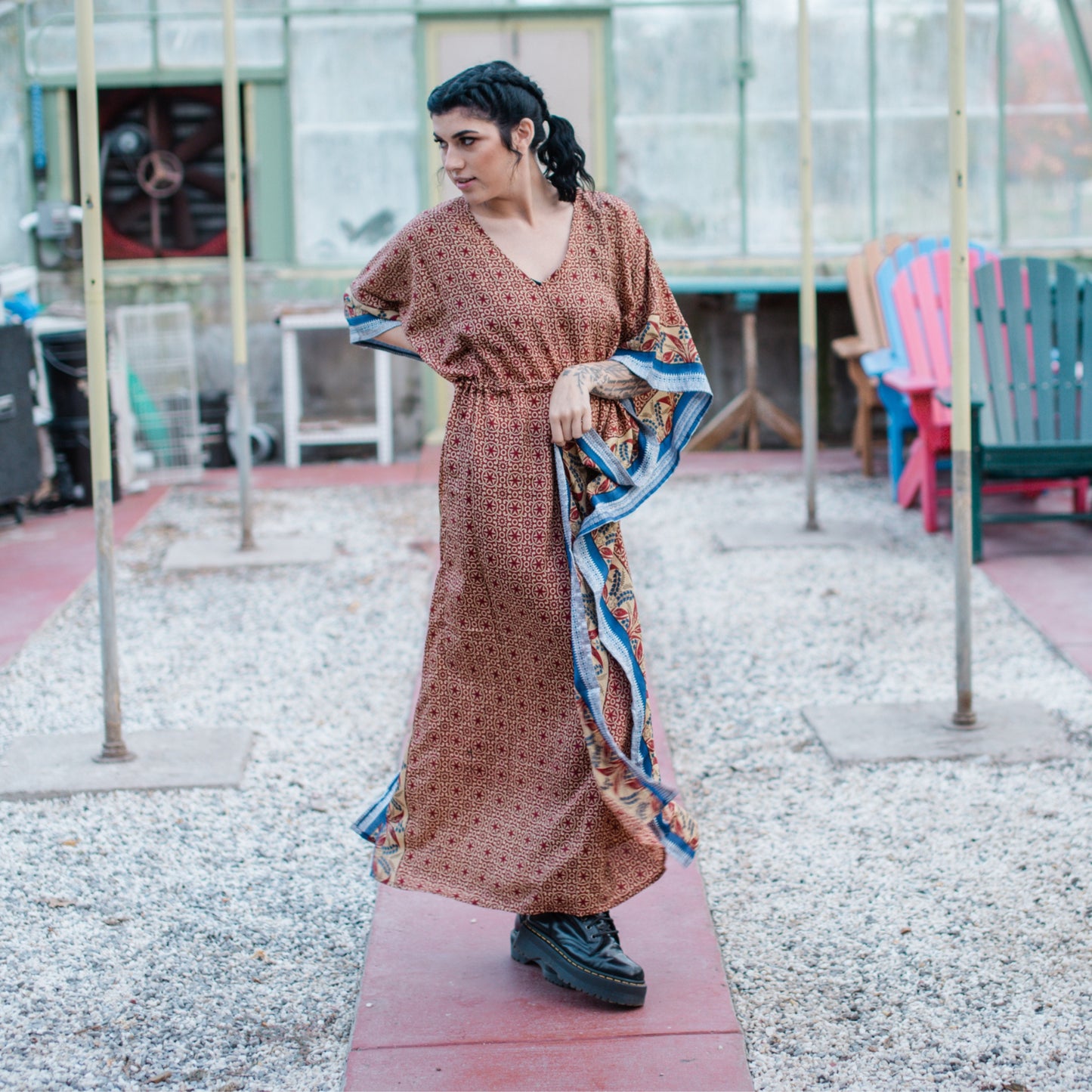 A model in a green house wearing a warm tones aanya long adjustable kaftan. This dress has blue and white along the flowy edges.