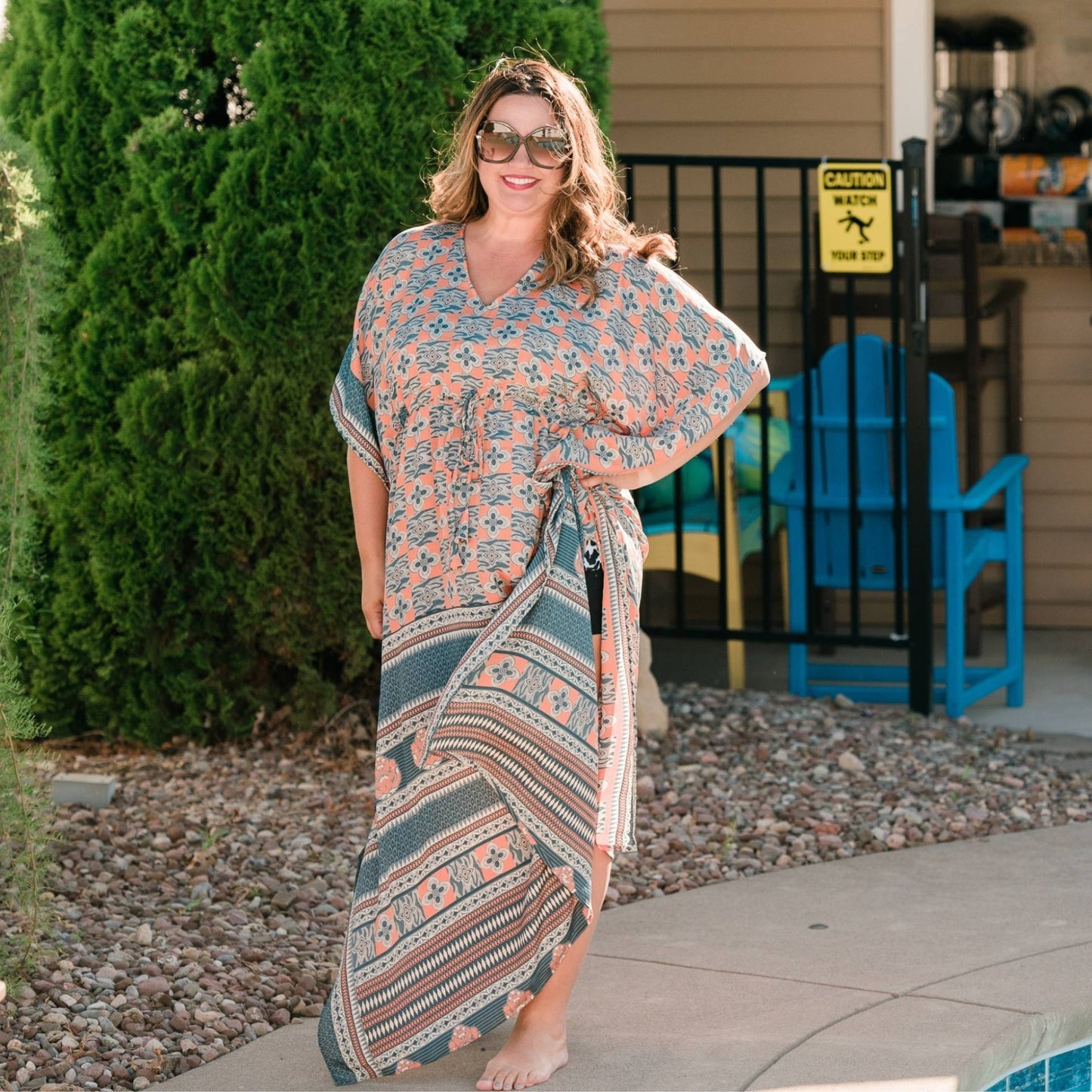 A woman by a pool wearing her reclaimed sari adjustable long kaftan as a bathing suit coverup. Her Aanya Kaftan is pale pinks and blues in tribal prints.