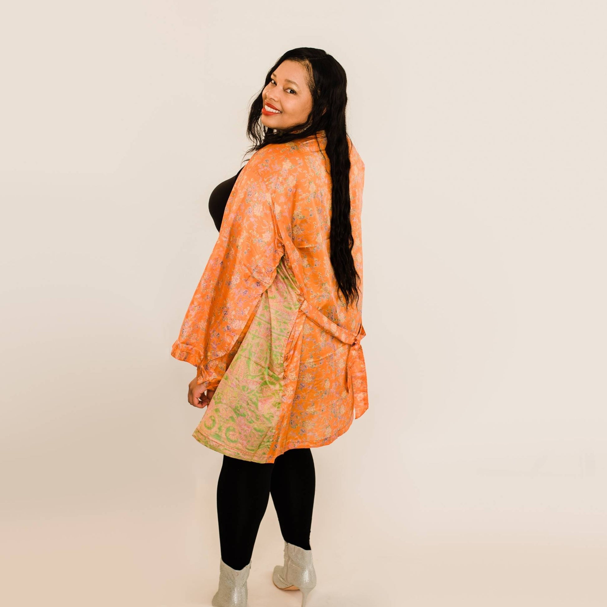 Model's back is to the camera with their head turned over their shoulder wearing an orange charlotte chic robe.