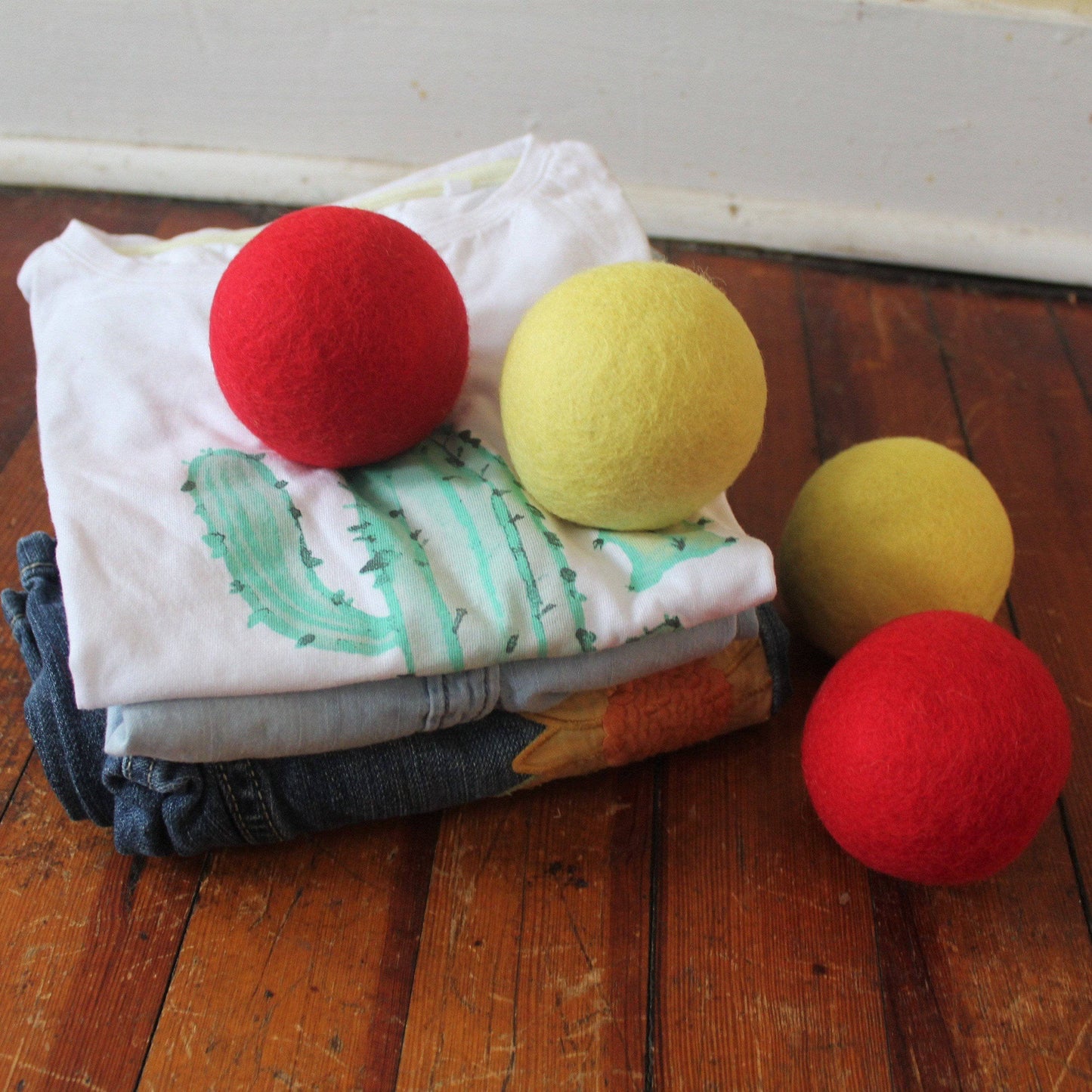 red and wool dryer balls pictured with folded clothing on wood background