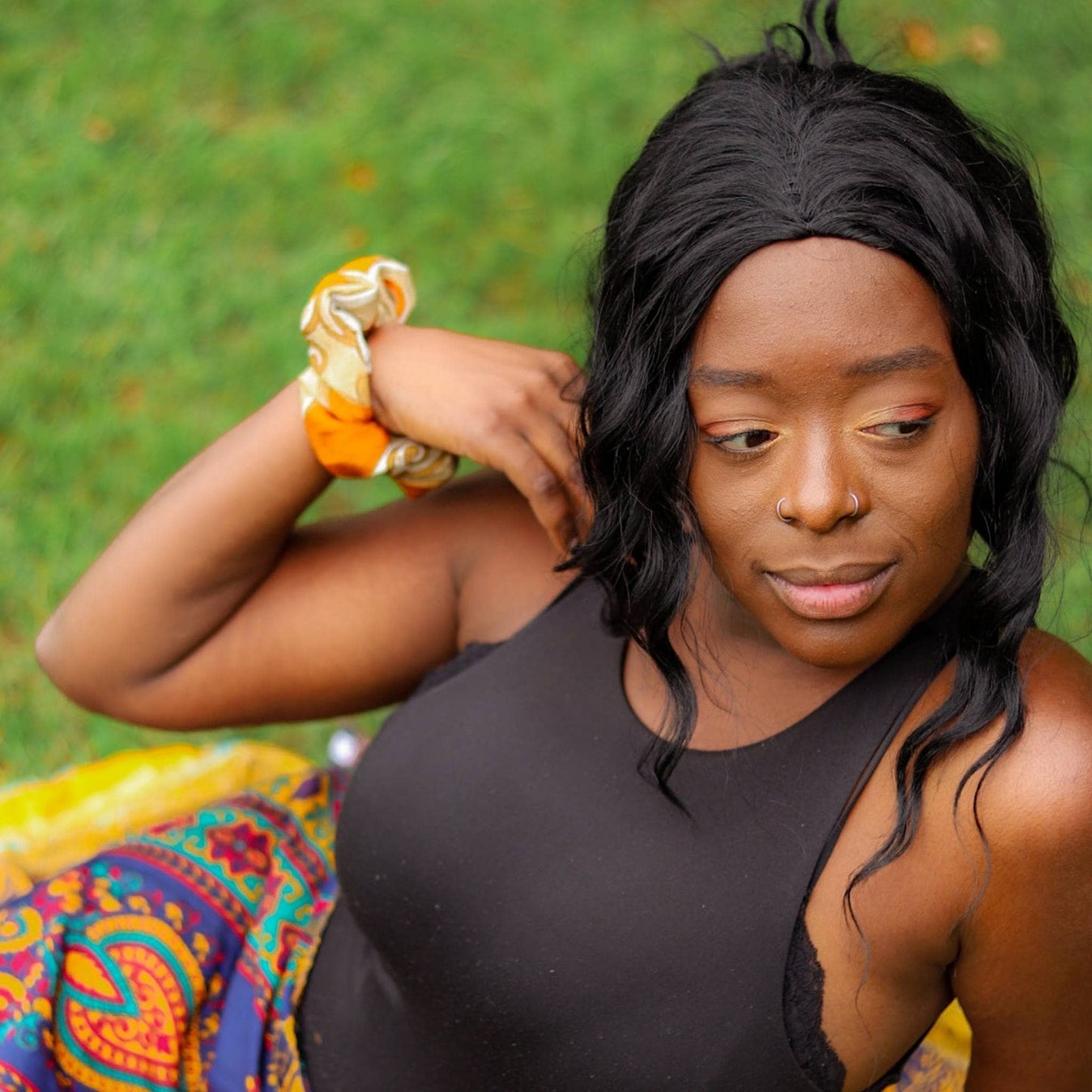 Model is laying in the grass with a sari silk srcunchie on their wrist.
