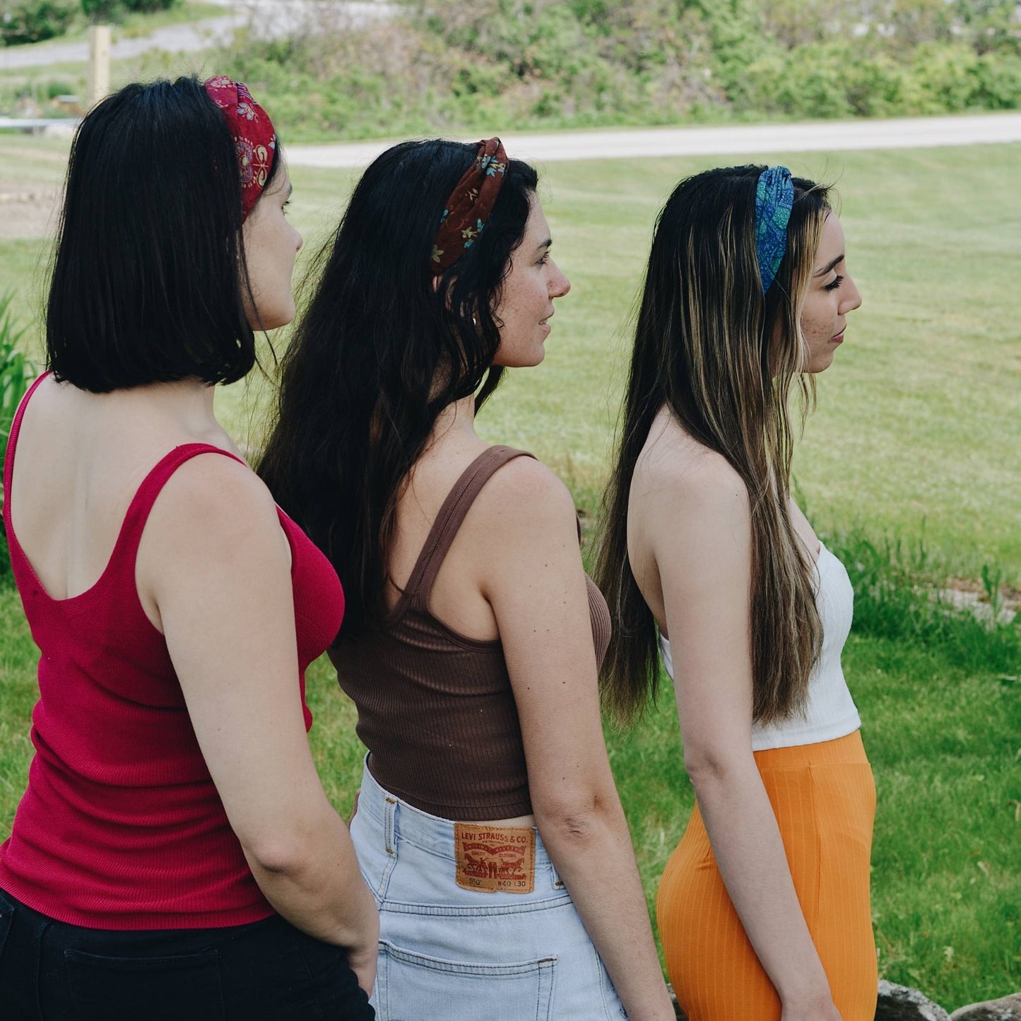 Three models standing with their backs to the camera wearing assorted kameela knot headbands