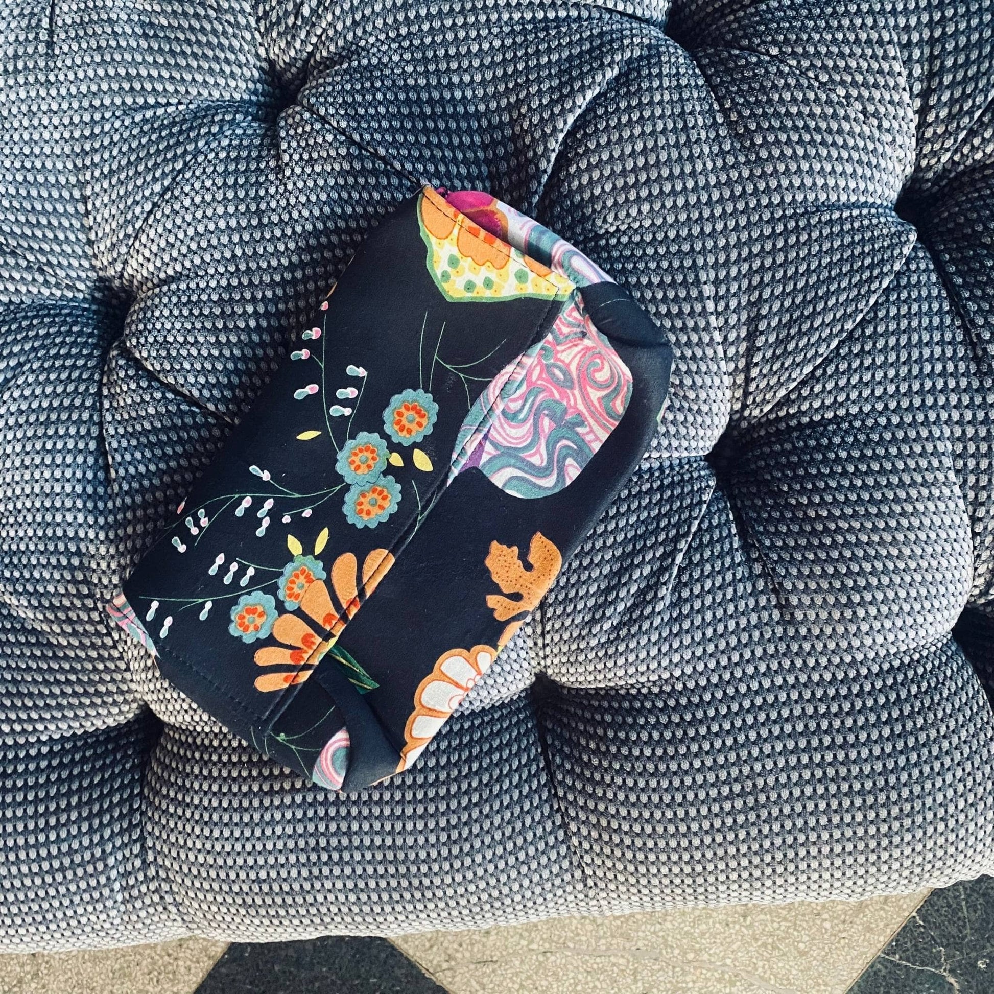 Black cotton clutch is sitting on a fabric grey bench.