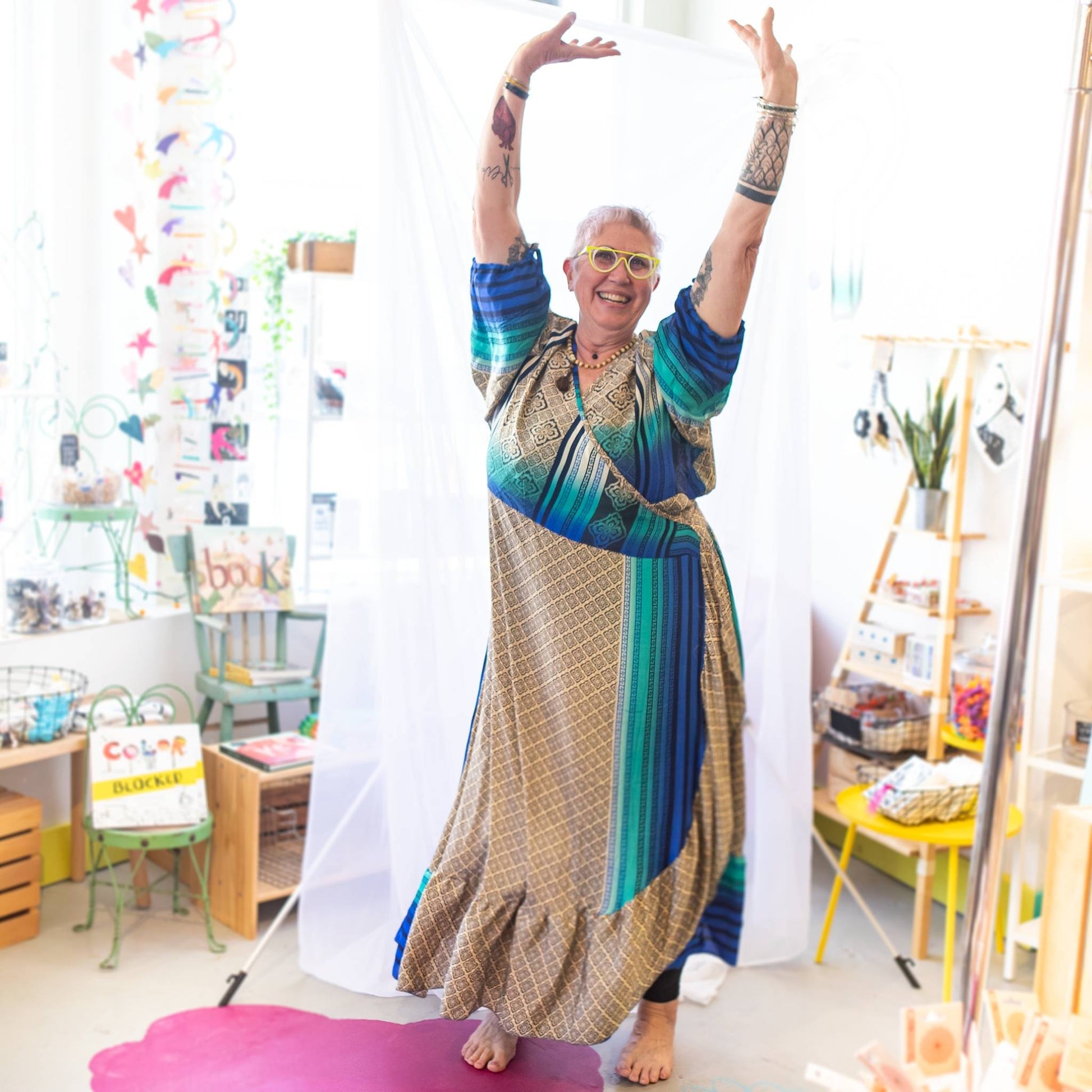 Model has their hands up above their head wearing a beige and blue zaria wrap dress while standing in a a bright room.