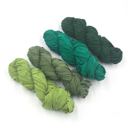 Chiffon Ribbon yarn is the colorway Jungle on a white background. These colors are light greens to forrest greens.