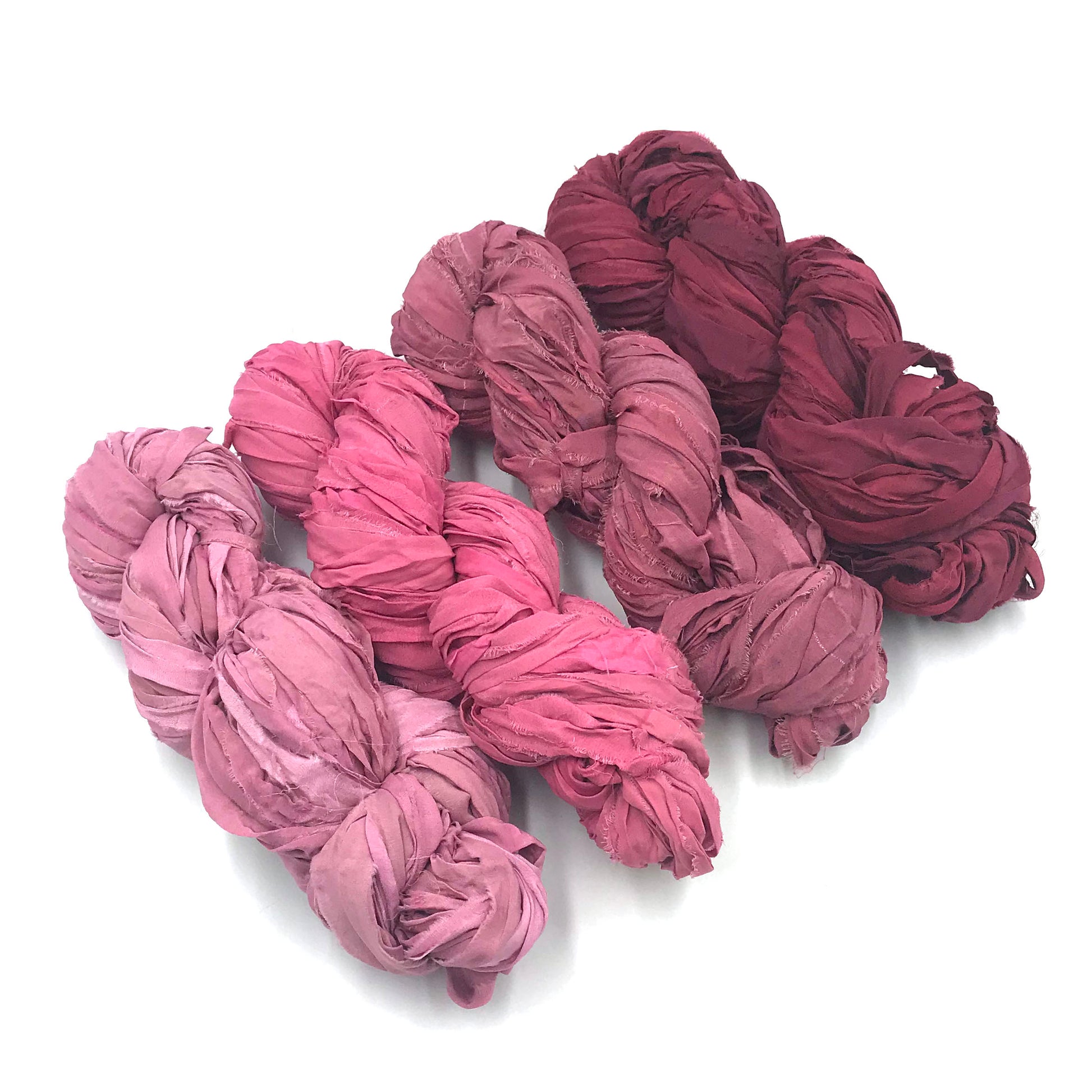 Chiffon Ribbon yarn is the colorway Lipstick on a white background. These colors are light pinks to blush red.