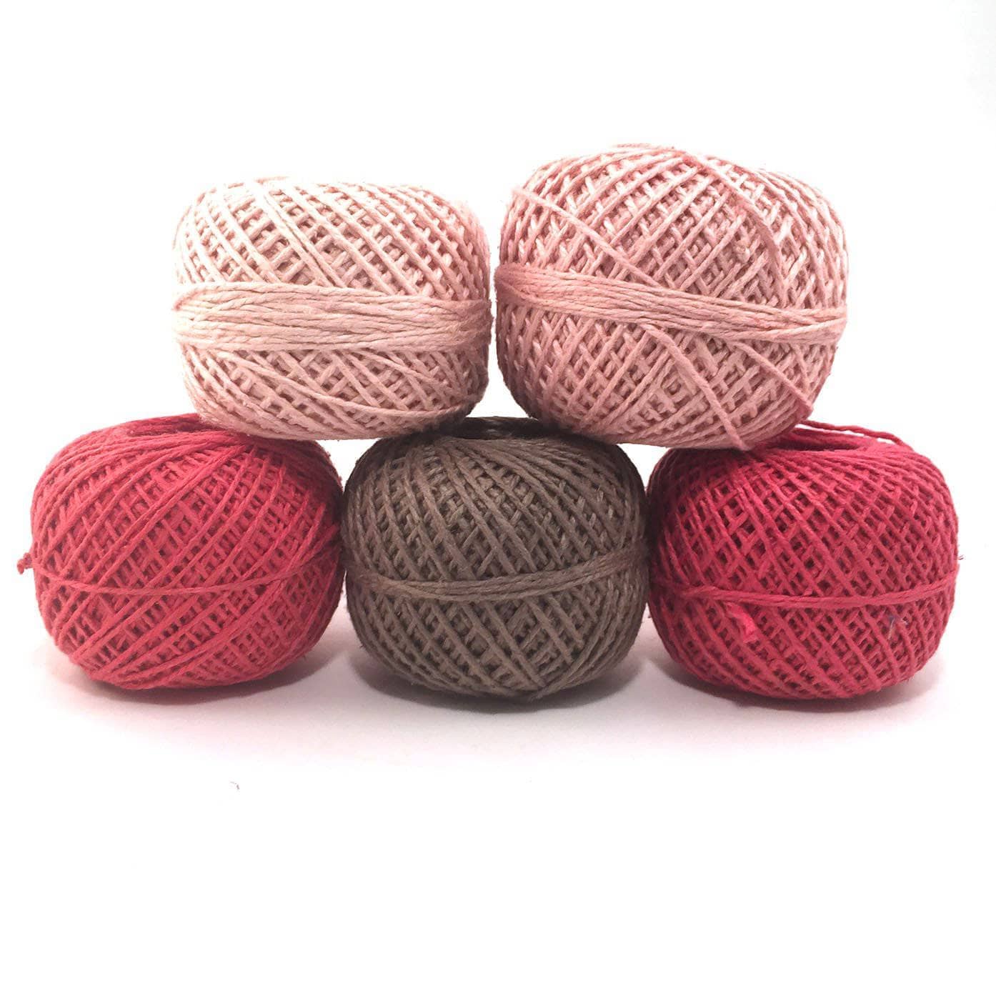 Herbal dyed recycled silk yarn pack in the colorway vintage rose in front of a white background. Blush pink, peachy pink, bright pink, vibrant pink, muted brown.