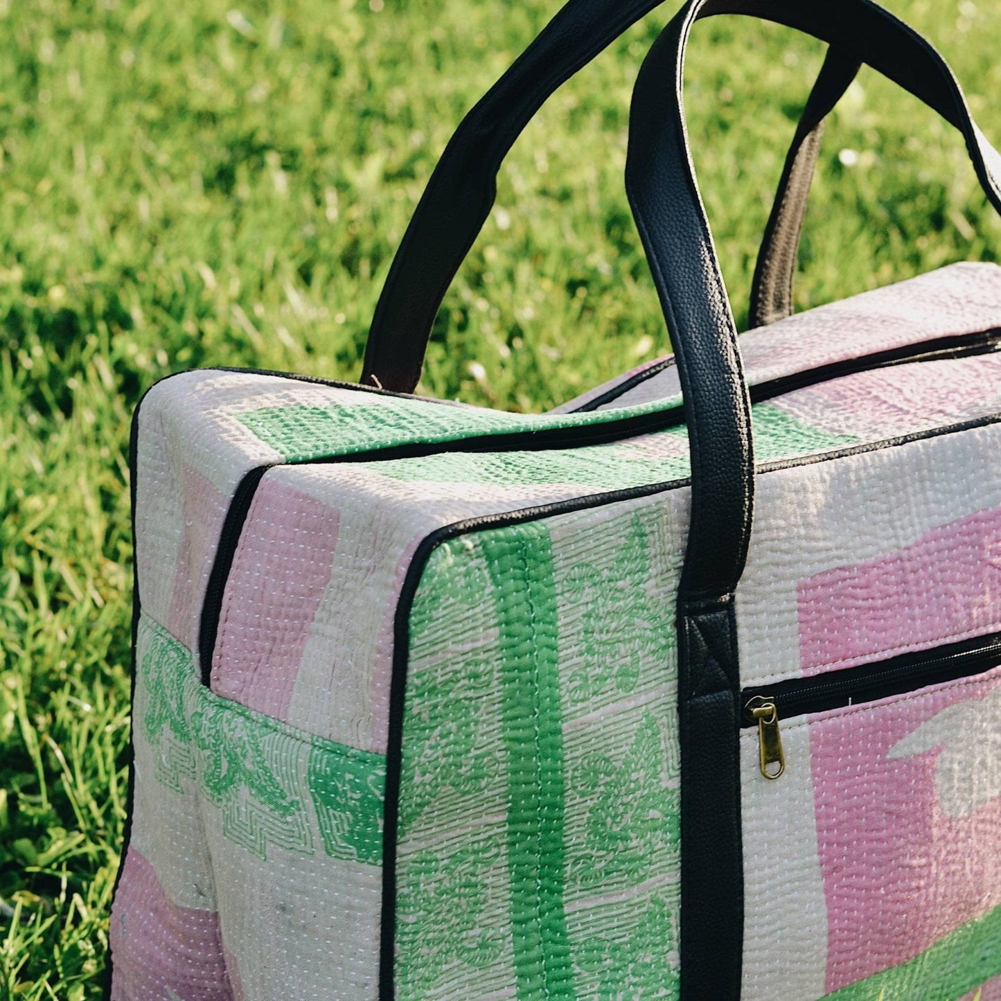 Close-up of green and pink kantha duffle bag sitting in the grass.