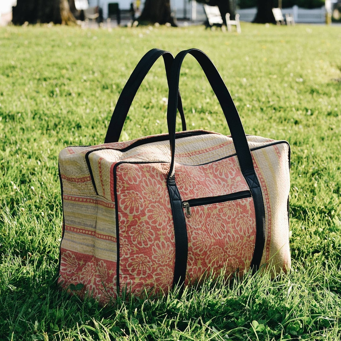 Orange and yellow kantha duffle bag sitting in the grass.
