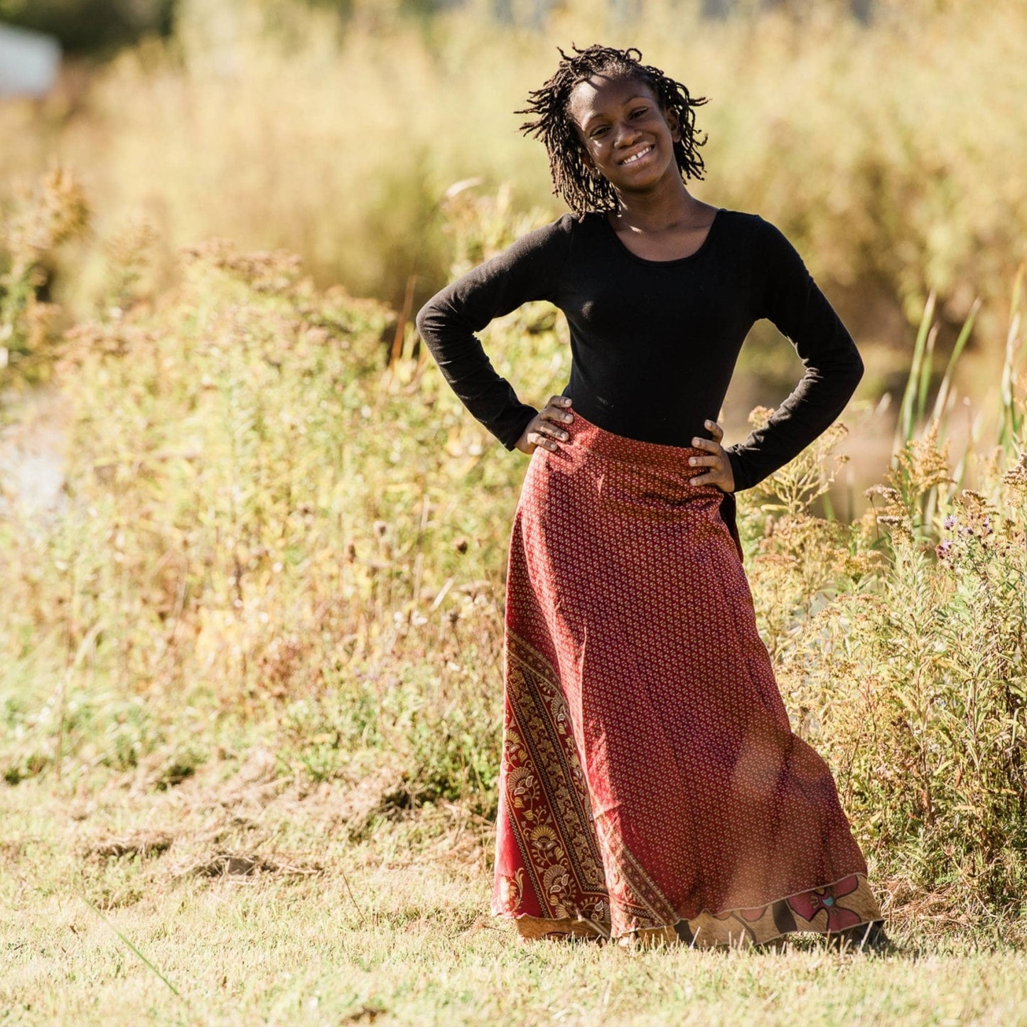 Junior model wearing a red maxi sari wrap skirt in a field.