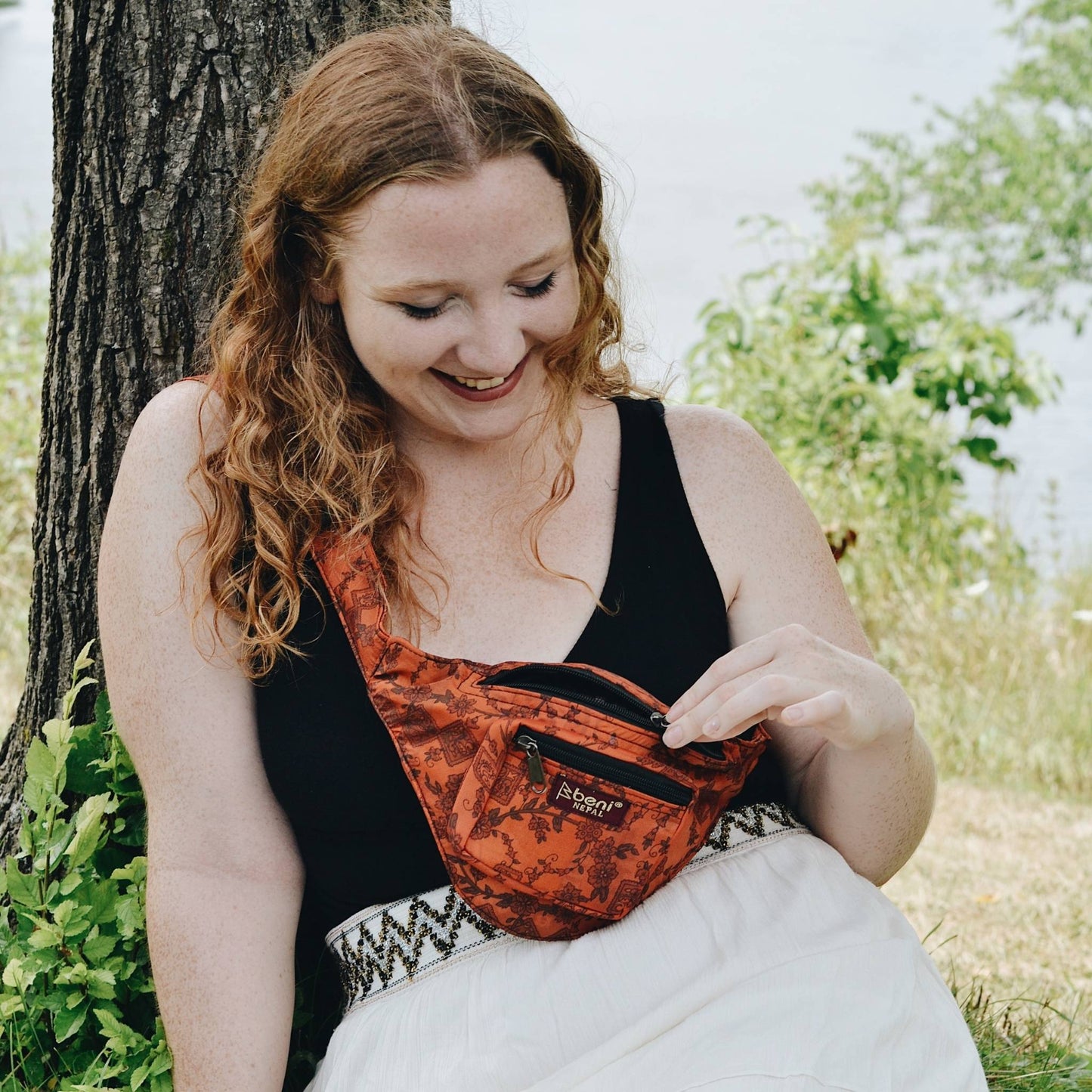 Model sitting by a tree wearing an orange fanny pack.