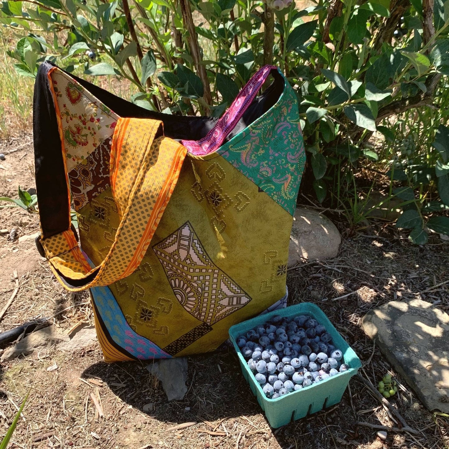 Sari silk purse is sitting on the grown outside with a carton of blueberries next to it.