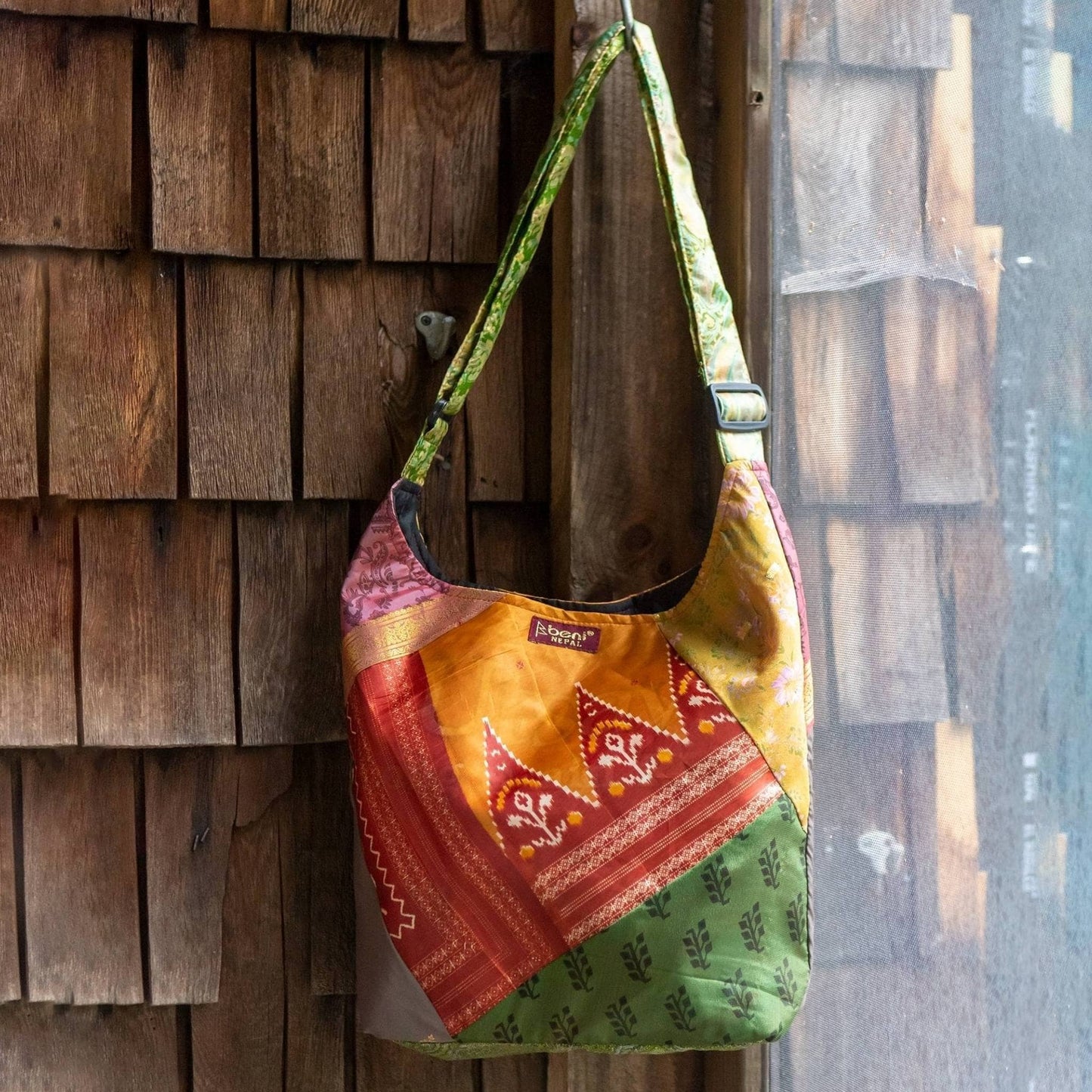 One of a kind sari silk purse hanging on a hook against a wooden house.