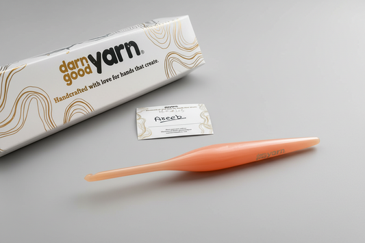 Orange crochet hook with 'darn good yarn' packaging on a light surface