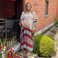 Smiling woman in a patterned kaftan posing near a brick building.