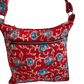 A red quilted bag with a floral pattern in blue and white. It has a front zipper pocket and an adjustable strap.