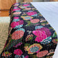 Night Lily Kantha quilt laying at the end of a bed with white bedding underneath. 