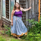 Model is standing outside next to a wooden building wearing a light blue ankle length sari wrap skirt.