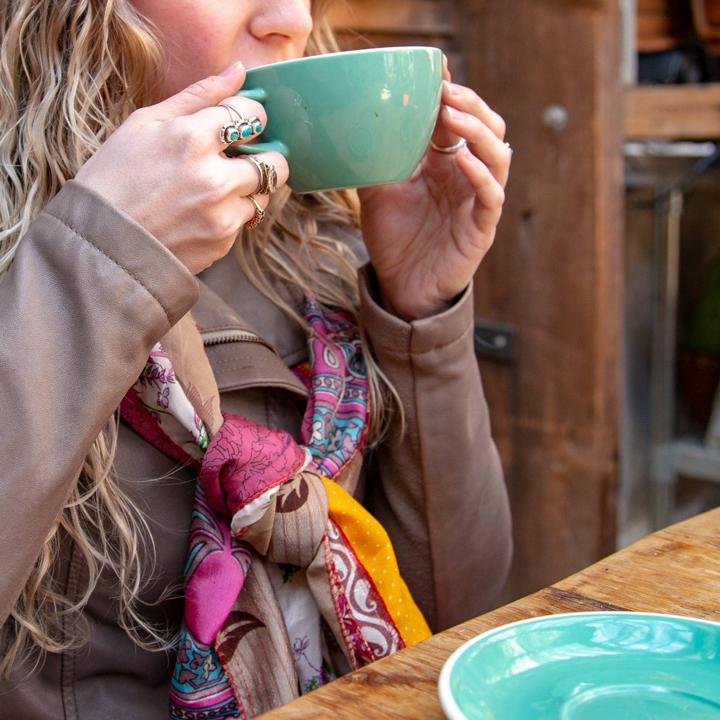 A woman drinking coffee with a colorful scarf and rings.