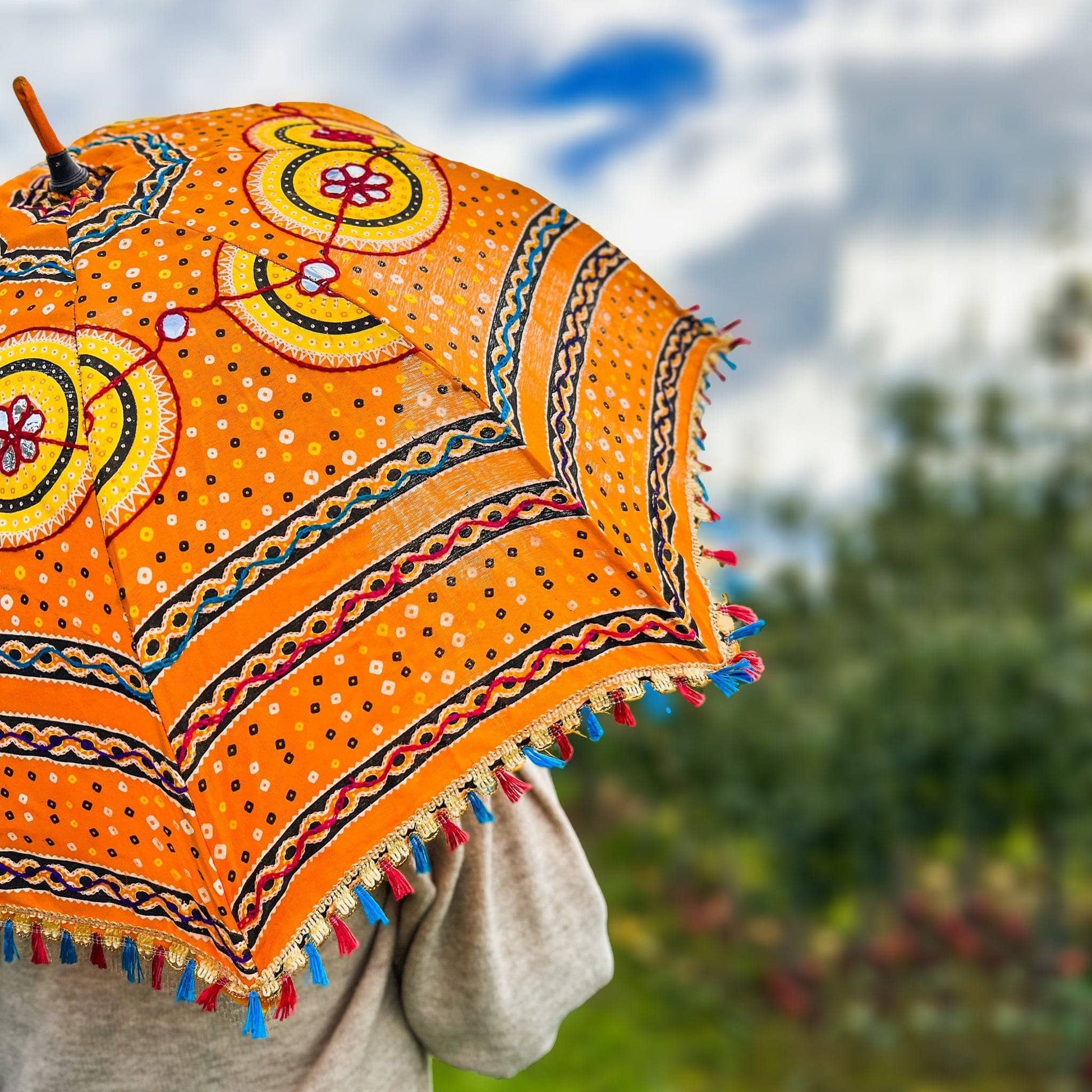 Model is holding an Embellished Parasol Umbrella with blurred trees in the background. 