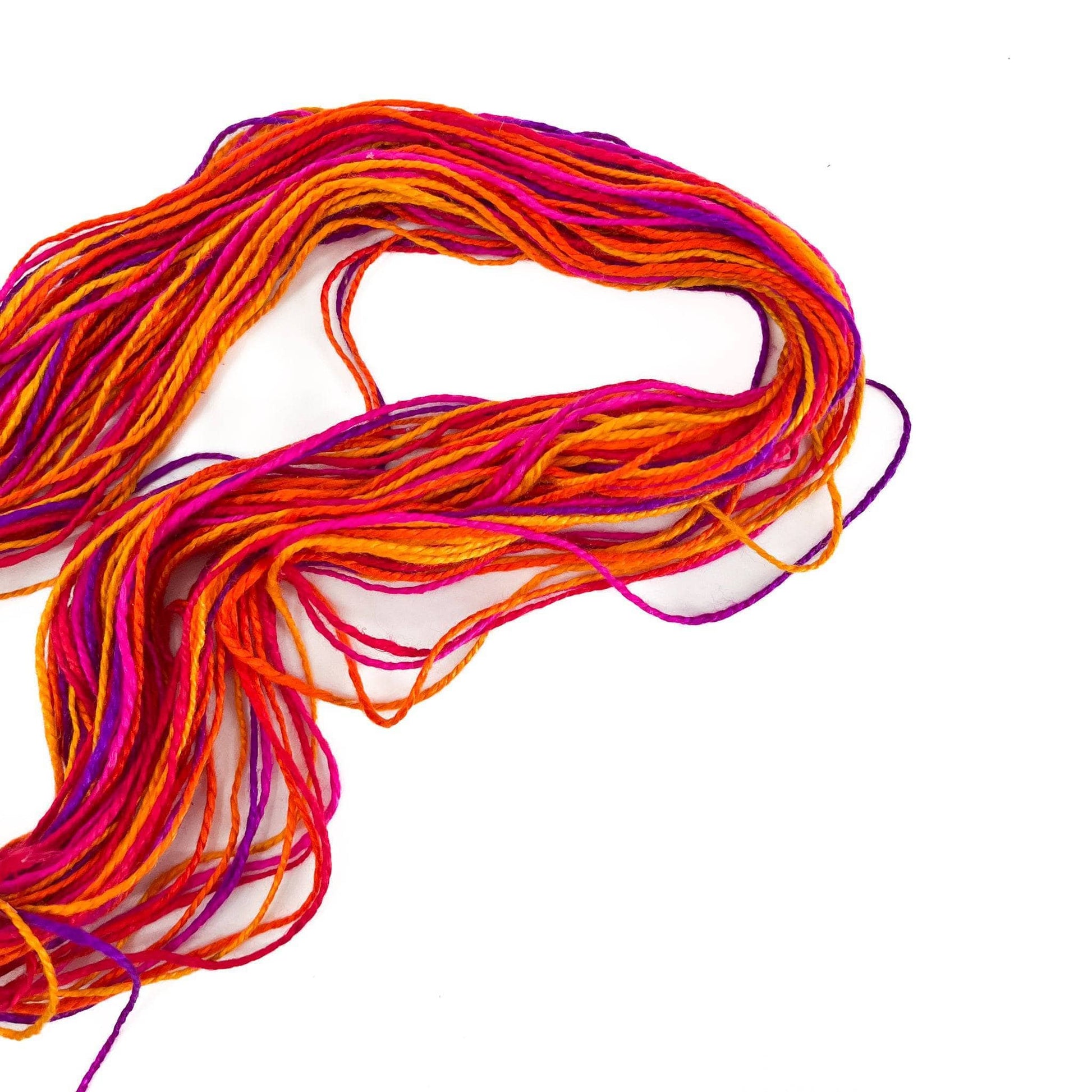 Unrolled skein of autumn Jubilee yarn (variegated hello, orange, purple, pink and red) spread out over a white background
