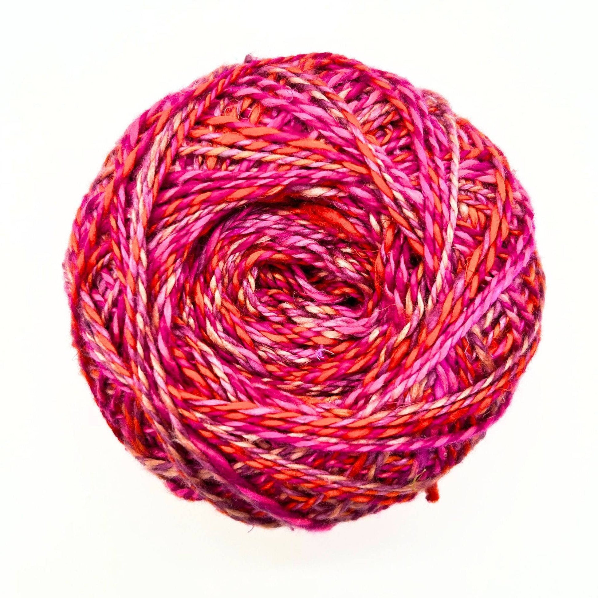 one skein of journey recycled silk yarn in the Field of Poppies colorway (variegated pink, orange, red) in front of a white background.