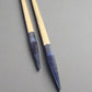 Two wooden brushes with blue-tinted tips against gray background.