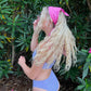 Model is wearing a pink furoshiki as a headband while standing in front of some tres outside on the beach. 