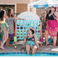 A group of models wearing assorted sari silk beach sarongs while standing a a pool with a giant game of connect 4. 