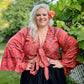 Smiling woman in a red top with flared sleeves, posing outdoors with a flower in her hair
