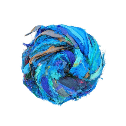 Single skein of windswept sari silk ribbon yarn turquoise in front of a white background. 