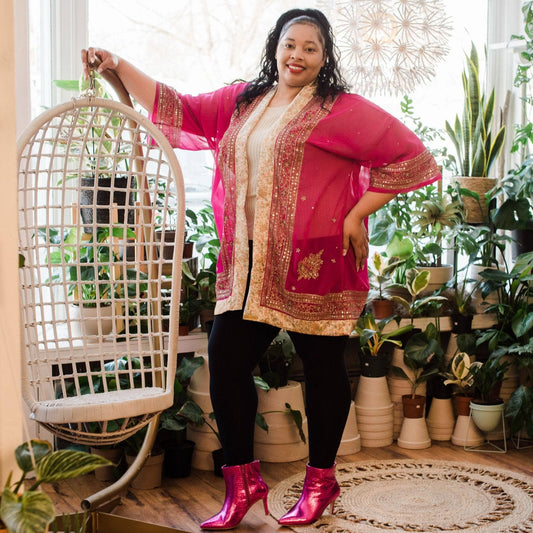 Model is standing wearing a pink sheer sophia silk duster in our goddess size next to a chair with potted plants in the background.