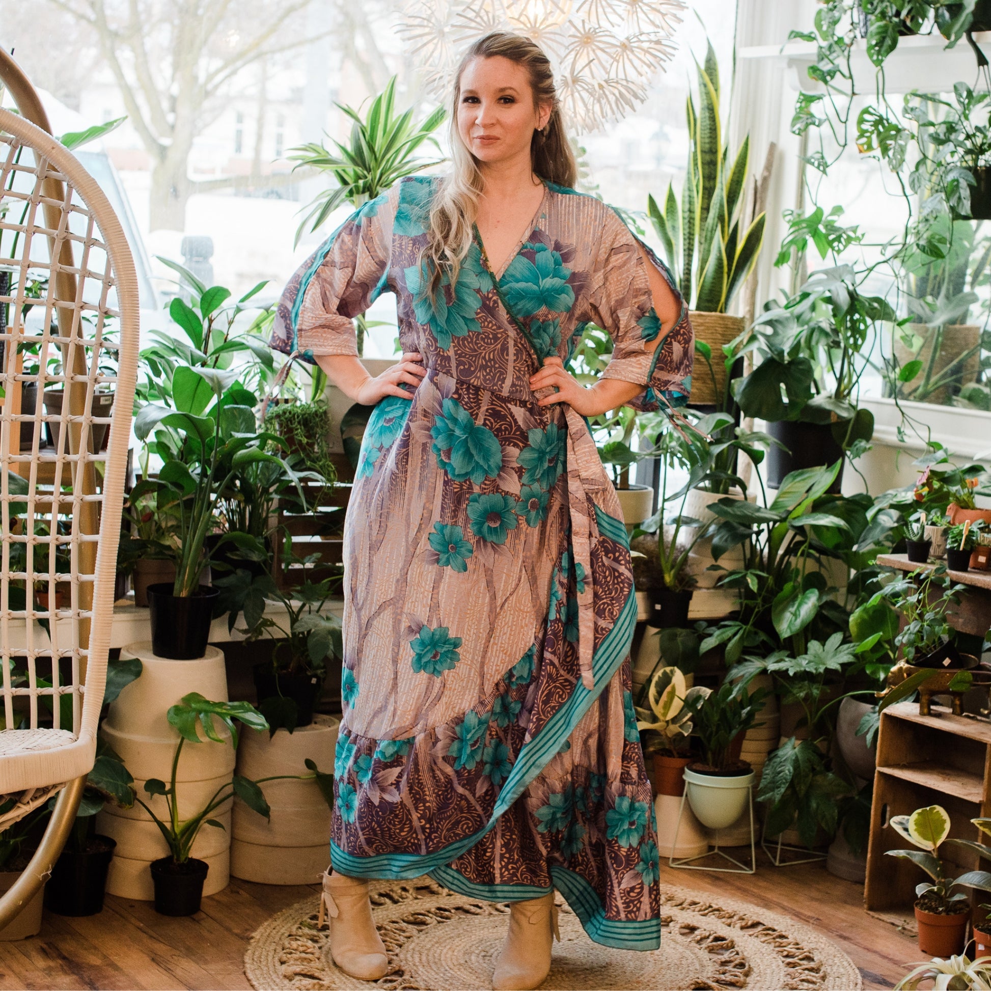A model standing with her hands on her hips wearing a Tan and Teal Blue Floral Zaria Wrap Dress. The Model is in a Flower Shop.