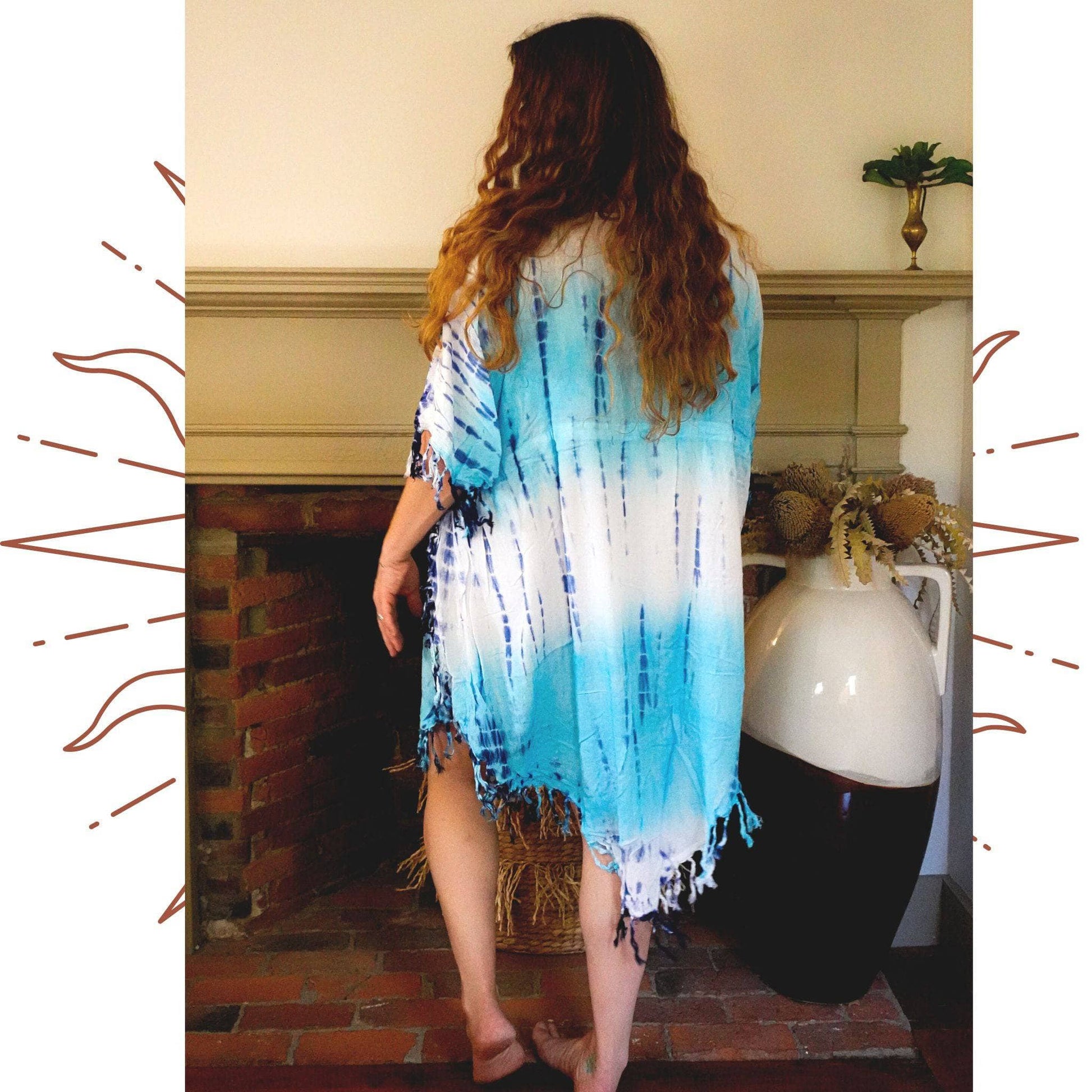 Nicole Snow wearing the tie dye sleep tunic in front of a fireplace with her back to the camera.