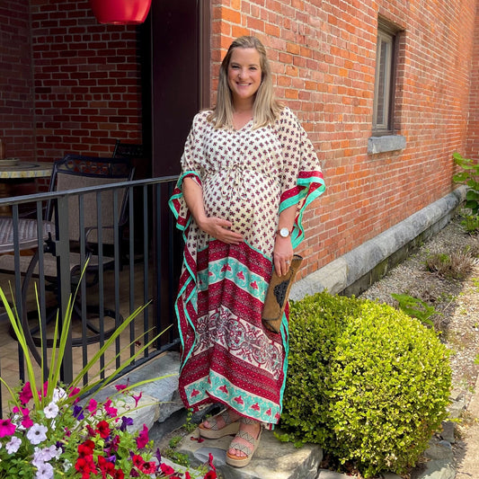 A Pregnant Woman attending a wedding as a guest. She's wearing a white patterned Aanya Adjustable Long Kaftan with hints of maroon and green. She's holding a matching clutch.