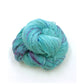 Sport weight silk yarn in Caribbean Current (turquoise and purple) in front of white background.