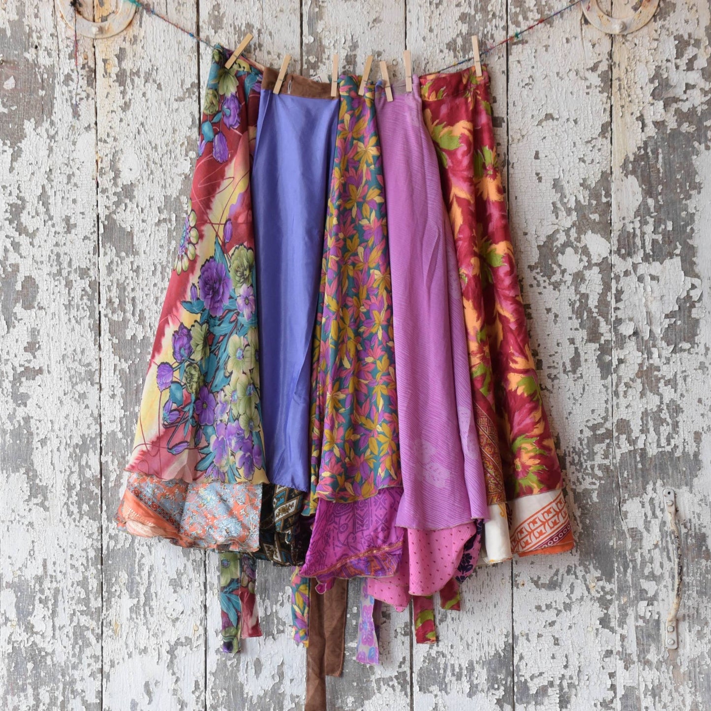 Colorful assortment of Sari wrap skirts hanging on a clothesline on a rustic wall.