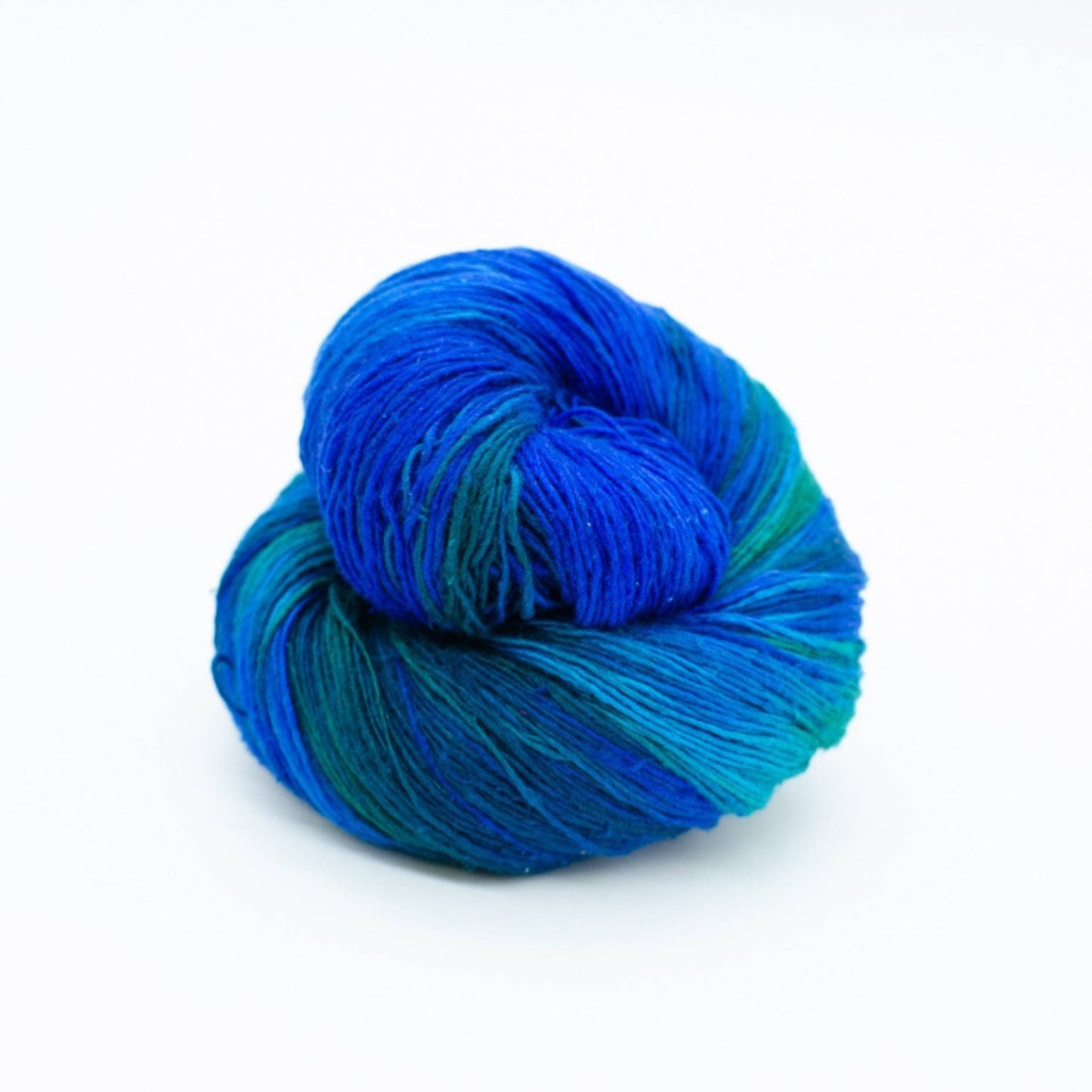 Lace weight silk yarn in color way Enchanted Forest (green and blue) in front of white background.