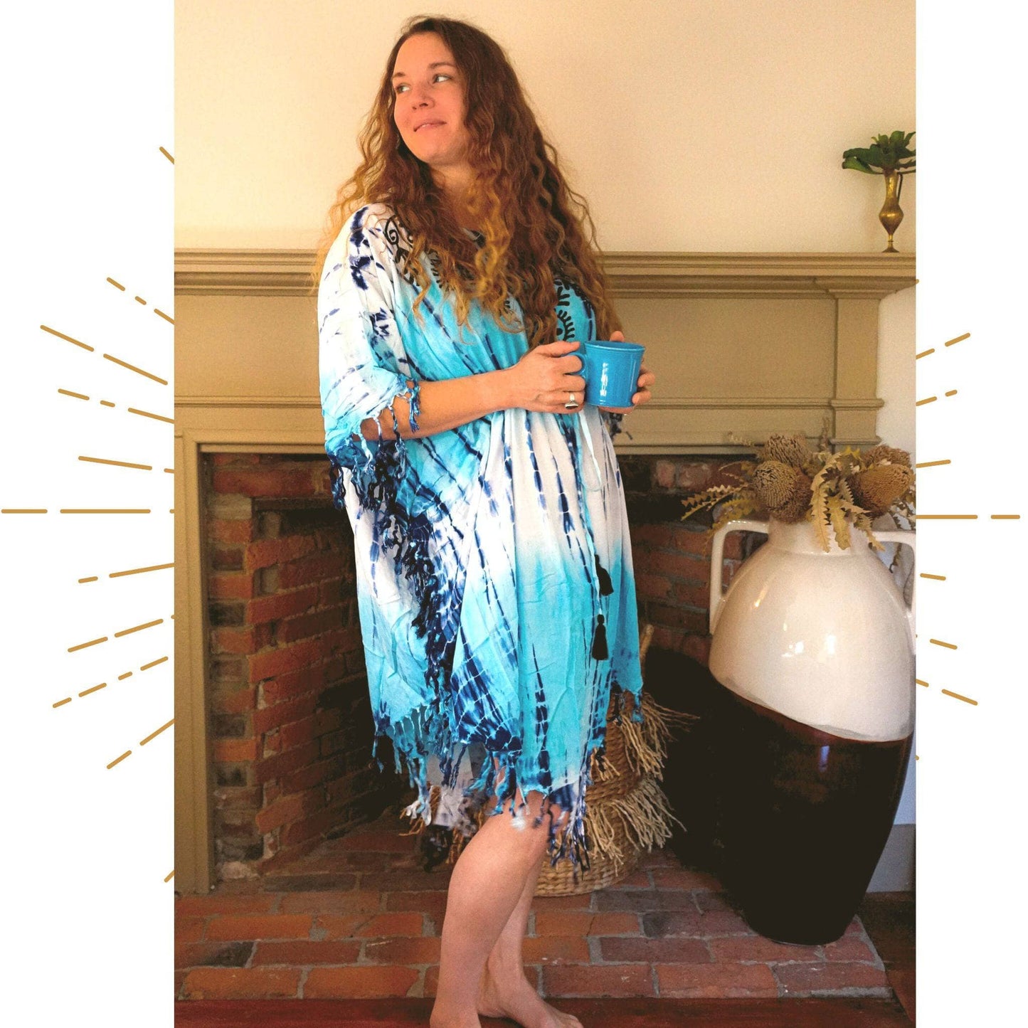Nicole Snow wearing the tie dye sleep tunic in front of a fireplace while holding a mug.